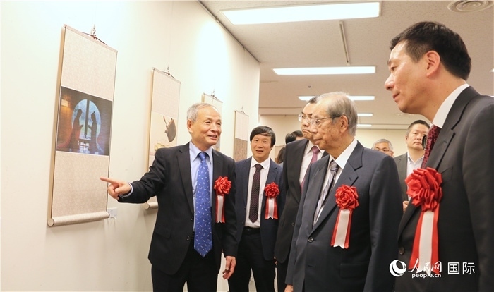 “湖州印象”攝影展主創(chuàng)、世界華人攝影協(xié)會(huì)副會(huì)長馮學(xué)敏向吳江浩大使、福田康夫前首相等嘉賓介紹展出作品。（人民網(wǎng) 許可攝）