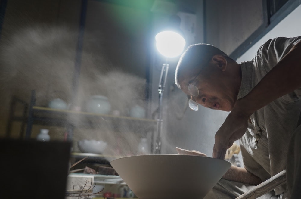 ↑ 在景德鎮(zhèn)，手工匠人吹去坯內(nèi)的泥土（2021年7月14日攝）。