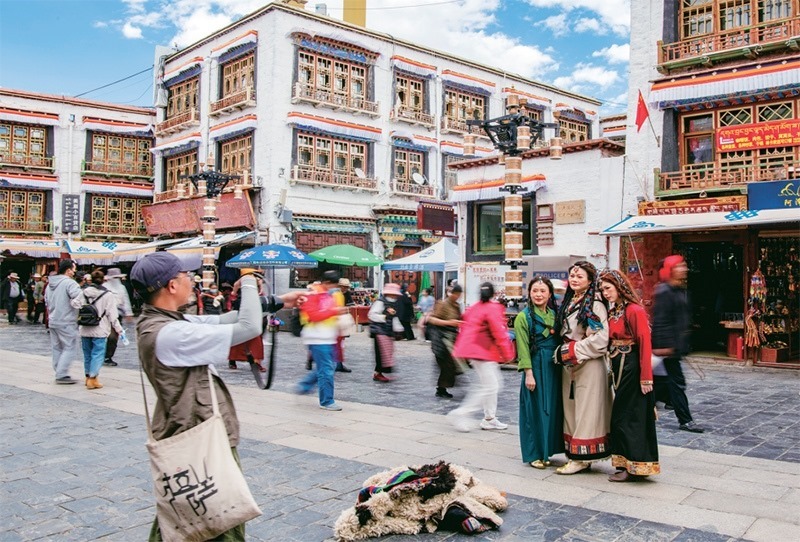 千年八廓街，見證民族團結(jié)。2021年7月，習近平總書記來到位于西藏拉薩老城區(qū)的八廓街，感慨地說：“千年八廓街，是我們各民族建起來的八廓街。各民族文化在這里交流交往交融，我們中華民族的大家庭在這里其樂融融?！眻D為2023年6月13日，游客身著藏裝在八廓街拍照留念。 新華社記者 姜帆/攝