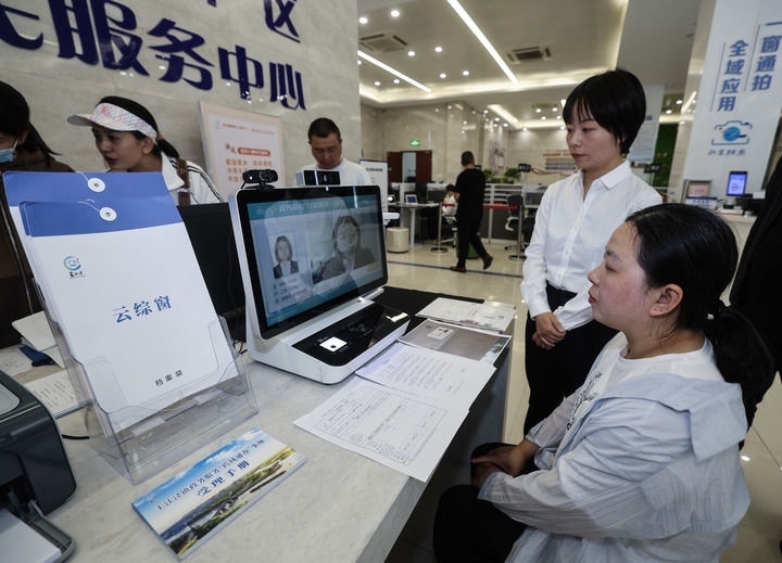 在浙江省嘉興市秀洲區(qū)王江涇鎮(zhèn)便民服務中心的“跨域通辦·云綜窗”窗口，辦理開業(yè)登記的個體工商戶（右一）通過該系統(tǒng)與江蘇省蘇州市吳江區(qū)盛澤鎮(zhèn)行政審批局工作人員視頻連線，進行身份讀取及材料線上審核（2024年5月9日攝）。新華社記者 徐昱 攝