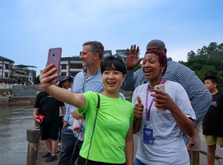 2024“一帶一路”媒體合作論壇聯(lián)合采訪調(diào)研行成員在樂山蘇稽古鎮(zhèn)與游客合影留念。本報記者 伊霄攝