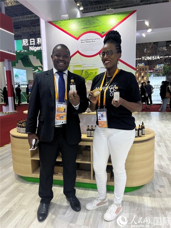 6月6日，布隆迪駐華大使館一等參贊布利馬索·阿爾弗雷德 (左，Bulimaso Alfred) 和參展商卡馬里扎·埃斯特拉 (Kamariza Estella) 在第七屆中國國際進(jìn)口博覽會布隆迪館展示當(dāng)?shù)厣a(chǎn)的辣木油。（人民網(wǎng) 艾里士 攝）